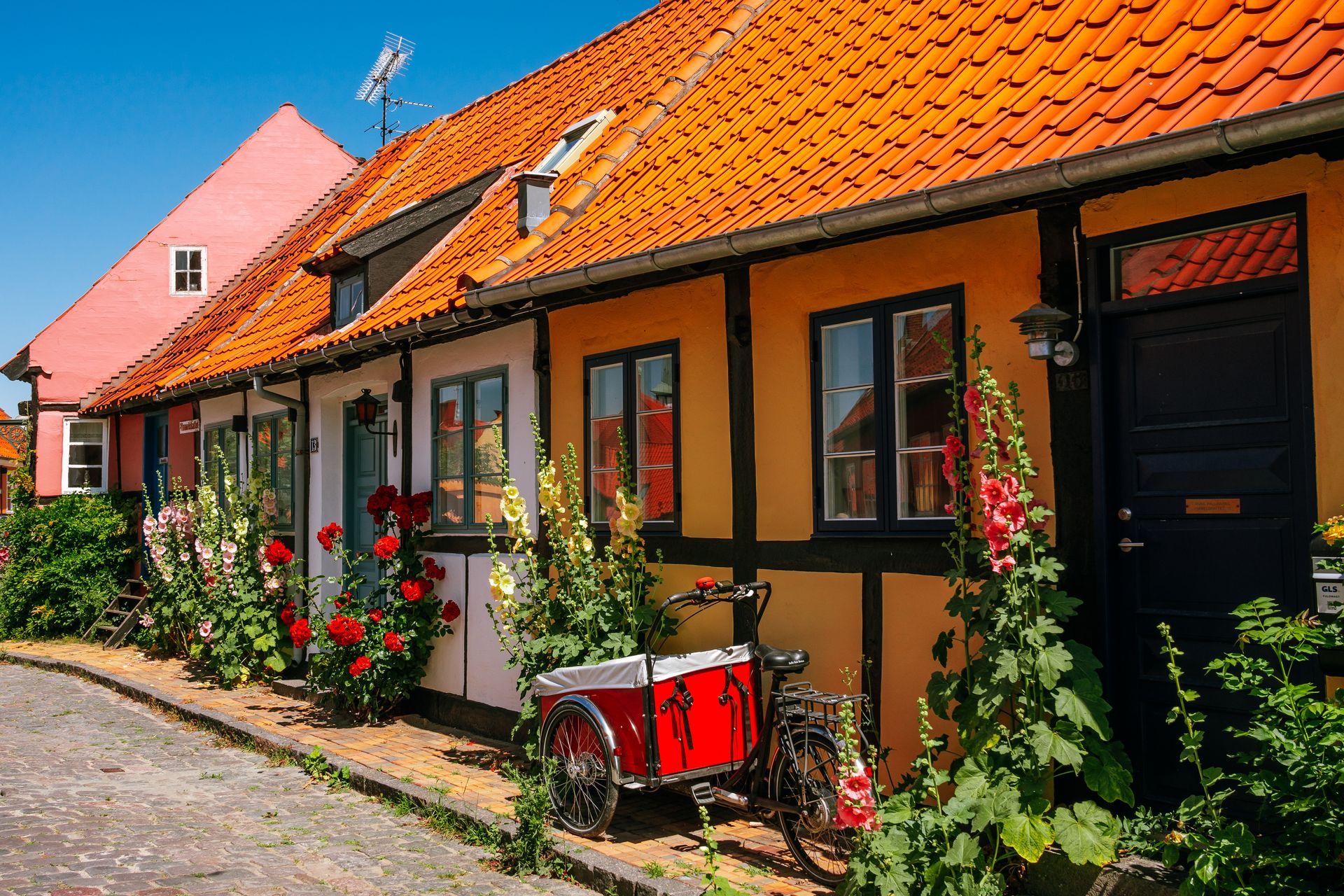 Yellow house and hollyhocks in Rønne, Bornholm Island in Denmark with bike and cart.