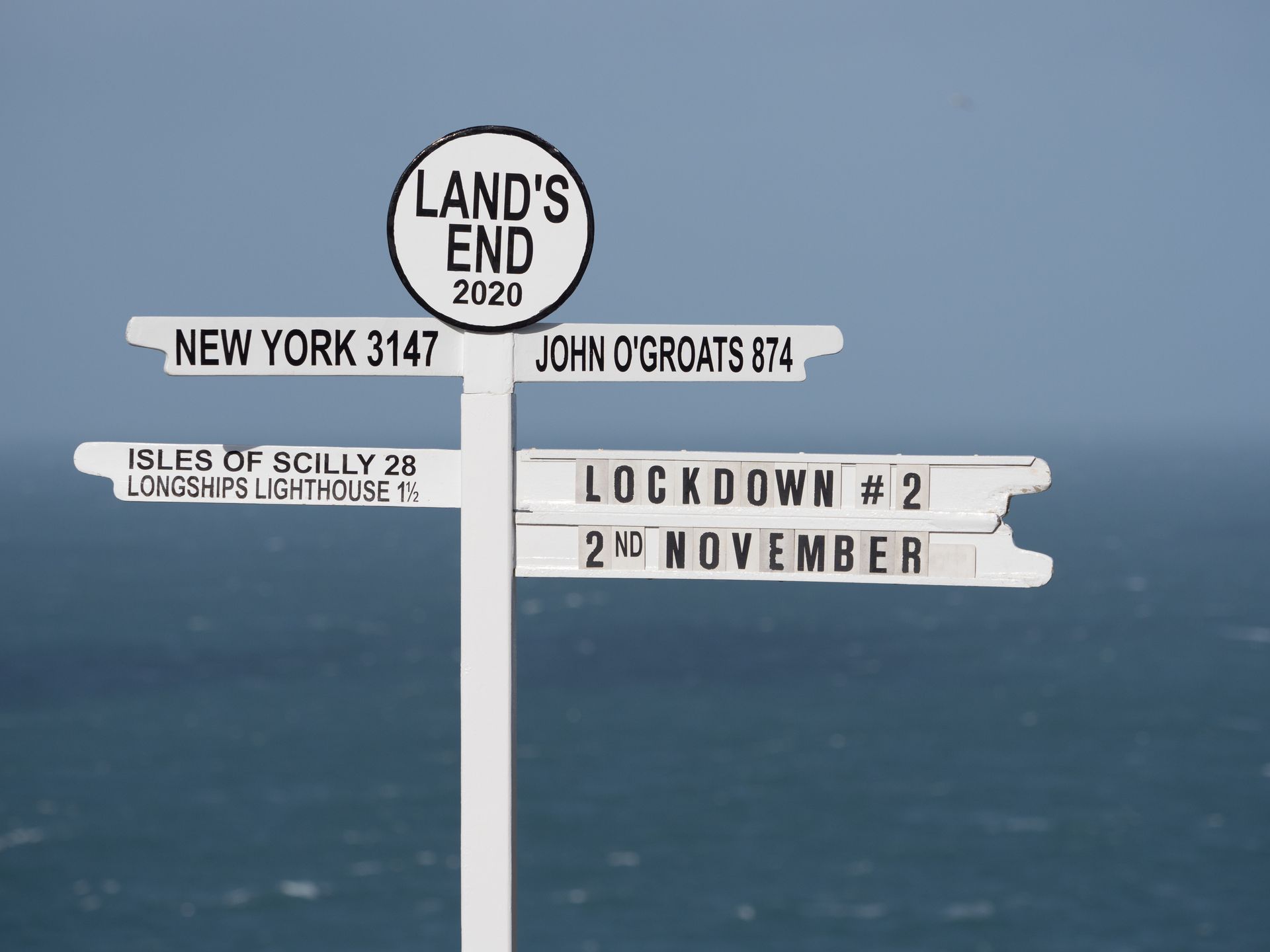 Iconic signpost at Land's End in UK has 'Lockdown#2' written on it indicating current affairs in UK Coronavirus epidemic restrictions.Sea in background