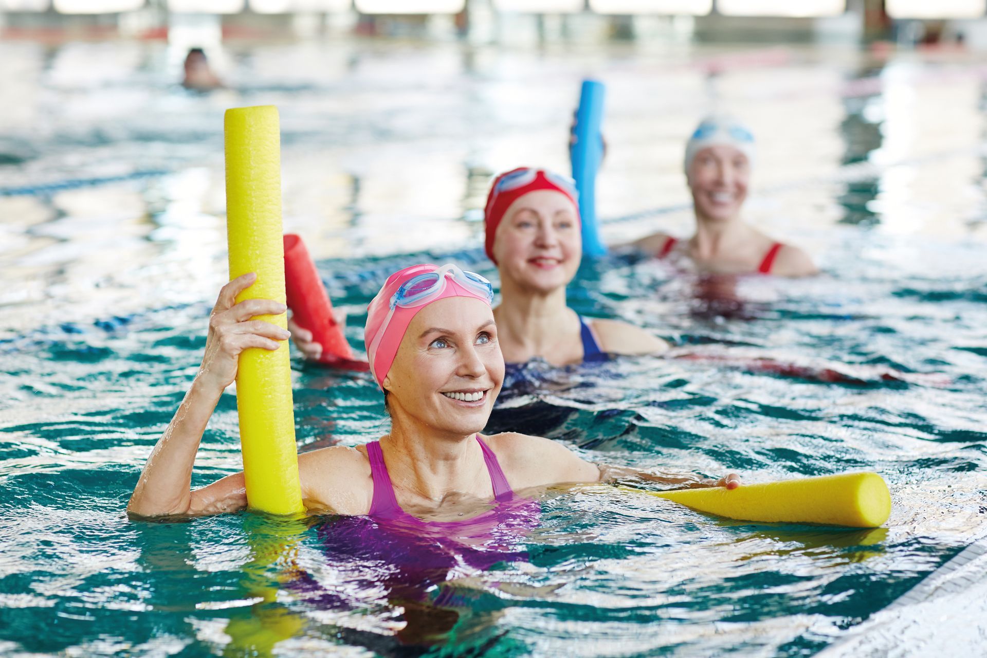 Smiling mature female in swimwear and two more active women listening to trainer advice during gymnastics in water