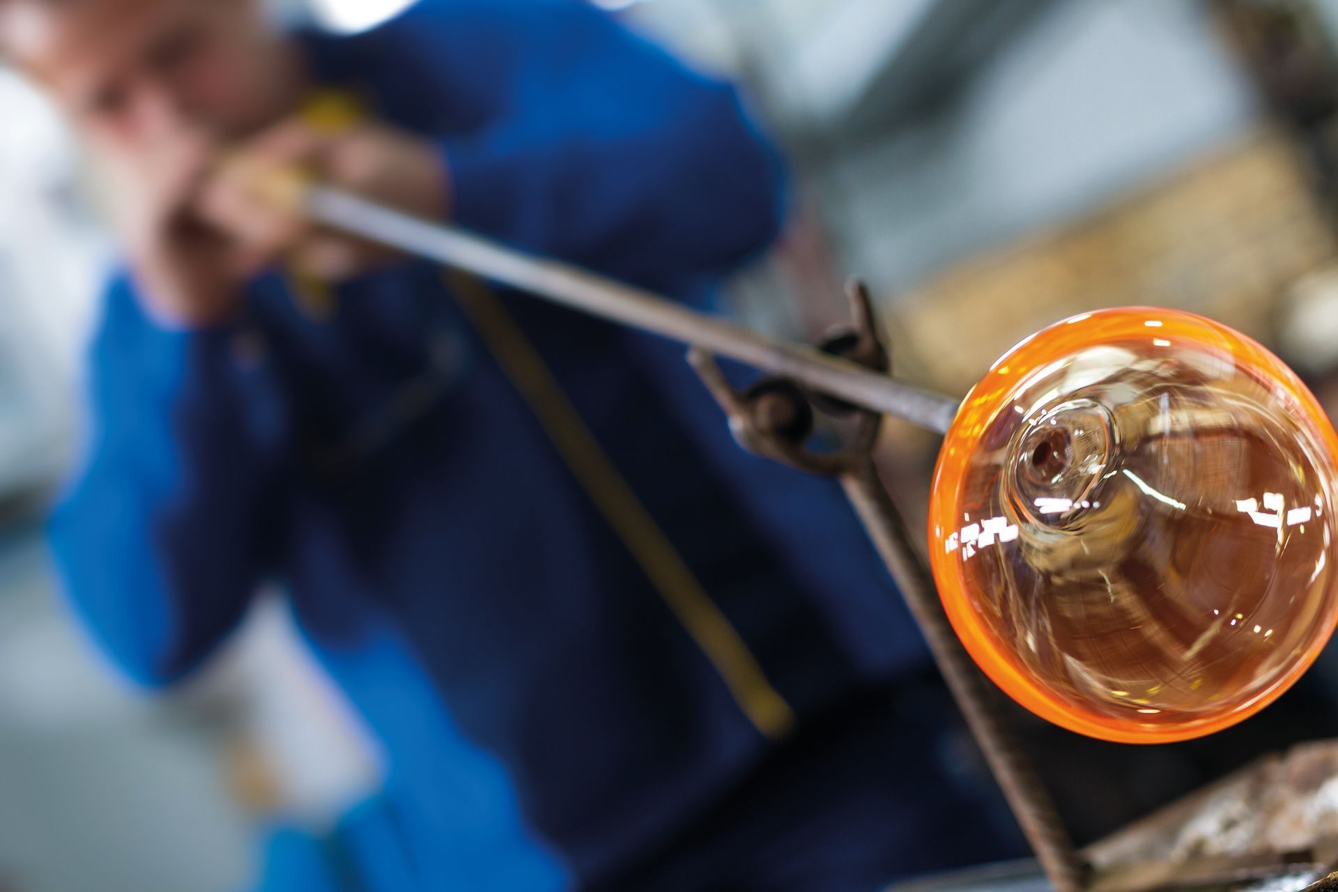Glass blower forming beautiful piece of glass. A glass crafter is burning and blowing an art piece.